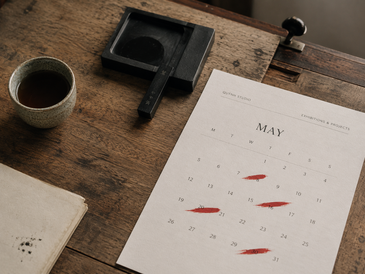 Calendar page with marked dates in vermillion brushstroke, single ceramic teacup, small ink stone on a vintage industrial drafting table, soft natural light